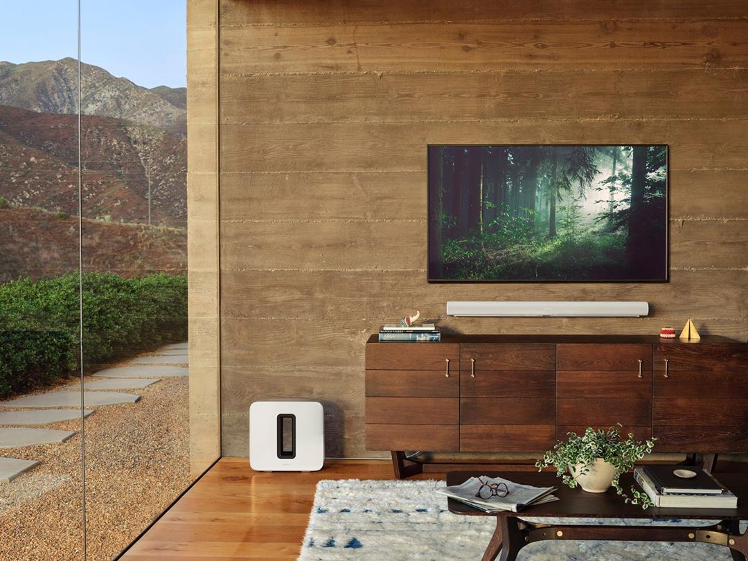 Living room interior features a media center with a flat-screen TV above a soundbar, a console, and an area rug on a wood floor.