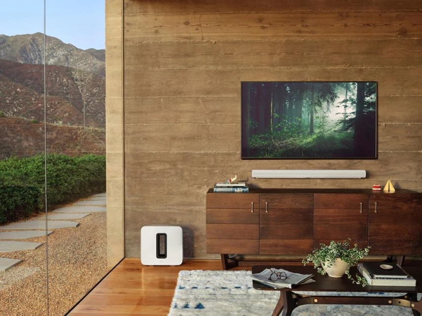 Living room interior features a media center with a flat-screen TV above a soundbar, a console, and an area rug on a wood floor.