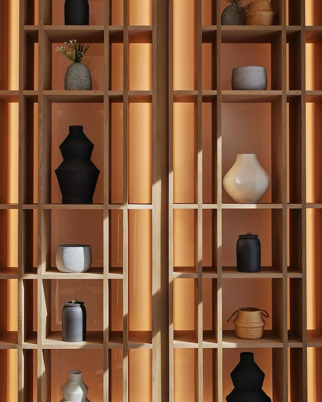 Wooden shelving unit with open compartments displaying an arrangement of decorative vases and vessels against a light orange background.