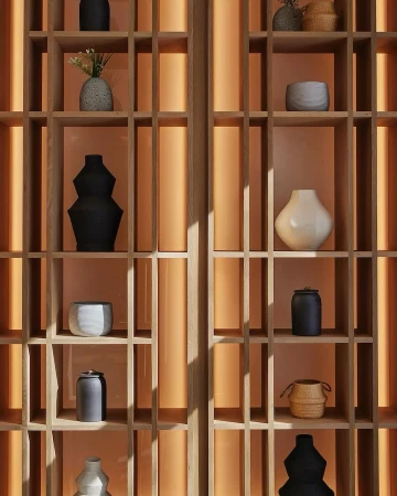 Wooden shelving unit with open compartments displaying an arrangement of decorative vases and vessels against a light orange background.