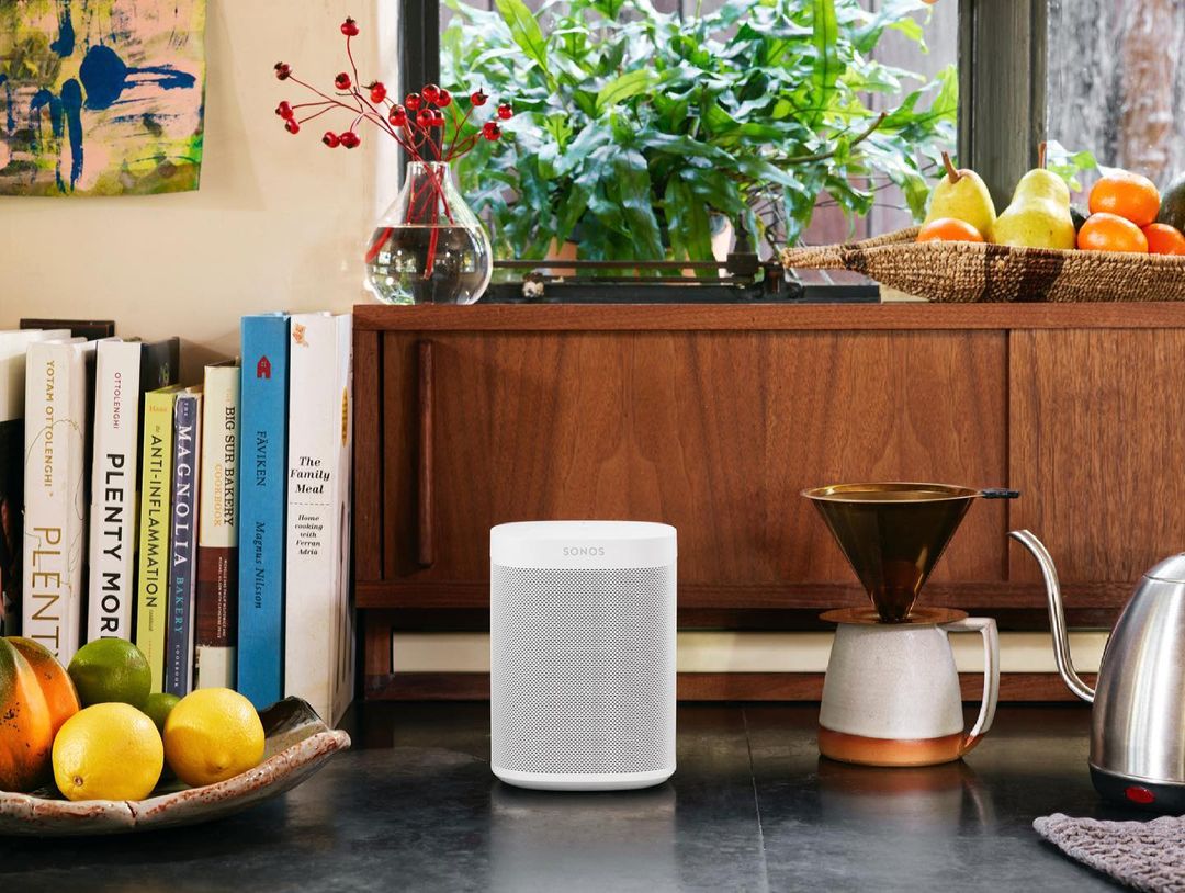 Indoor kitchen scene features a white SONOS speaker, books, and fruit. A vintage-style cabinet and coffee-making equipment adds warmth.