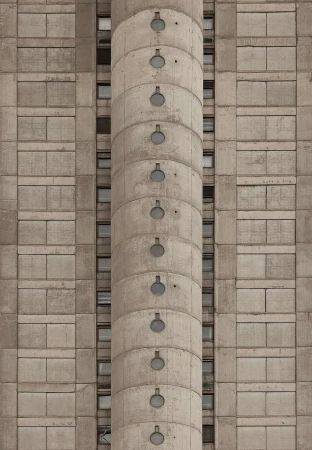 Concrete building facade with repeating geometric pattern and cylindrical tower featuring small, round windows running vertically.