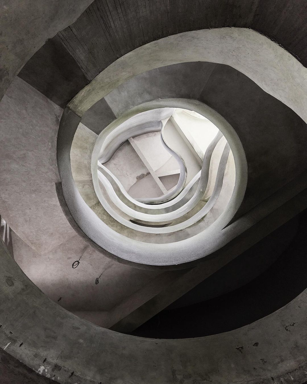 Concrete spiral staircase viewed from below, featuring a circular opening at the top and architectural design.