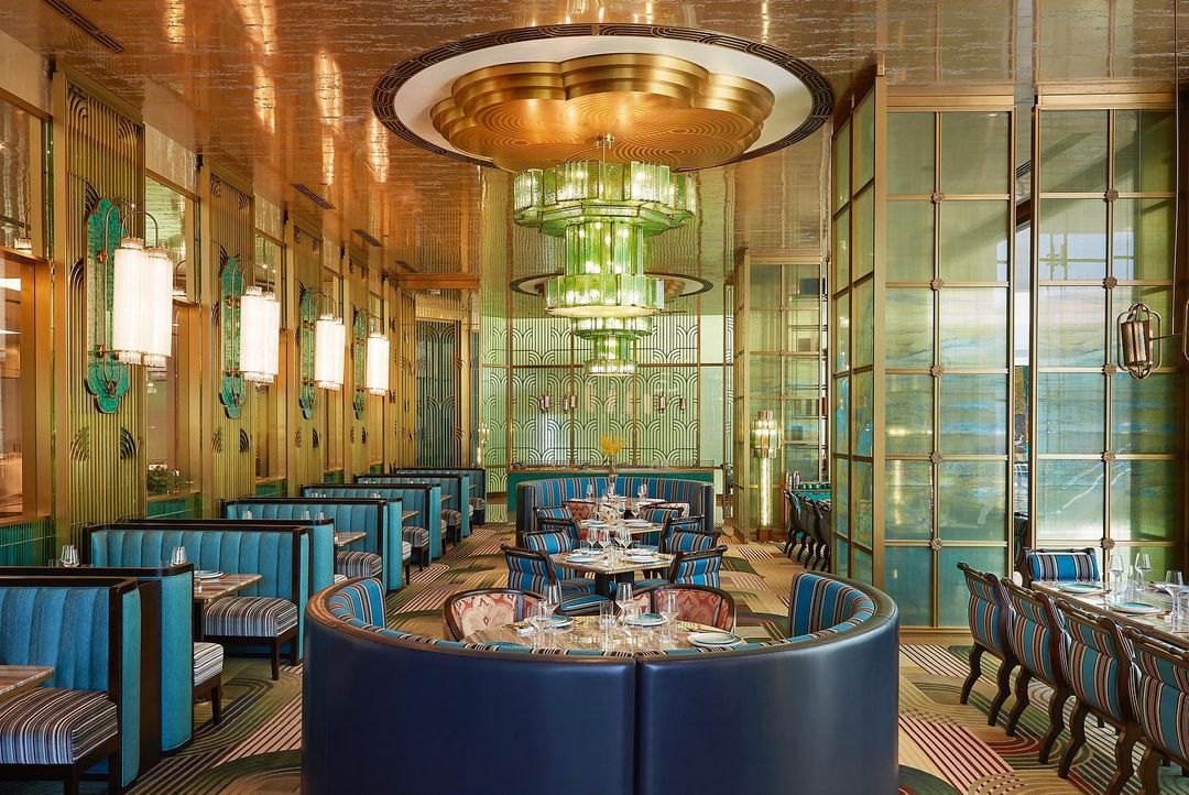 Ornate restaurant interior featuring turquoise and blue booth seating, tables set for dining, and a large, decorative chandelier.