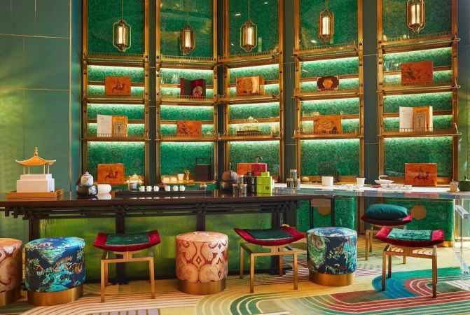 Interior of a tea room featuring a tea counter with stools, decorative objects, and a green display wall with shelves and lighting.