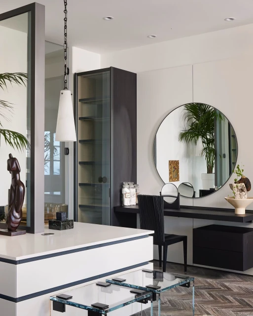 Interior view of a vanity with a round mirror, black chair, and decorative objects, in a room with natural light and neutral tones.