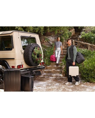 Two models pose with luggage and a luxury SUV in an outdoor setting with greenery and stairs, promoting travel and lifestyle.