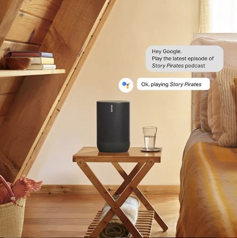 Smart speaker on a wooden table in a bedroom setting, alongside a glass of water and a shelf holding books, creates a cozy atmosphere.