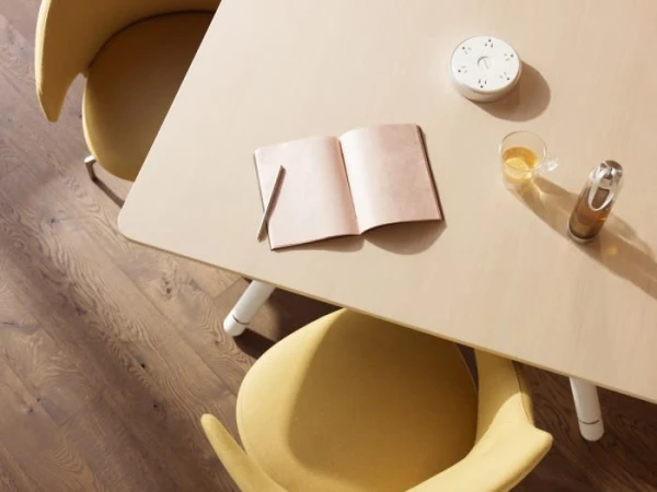 Overhead shot of an open notebook, pen, drink in glass, and bottle on a table next to two chairs with wooden floor background.