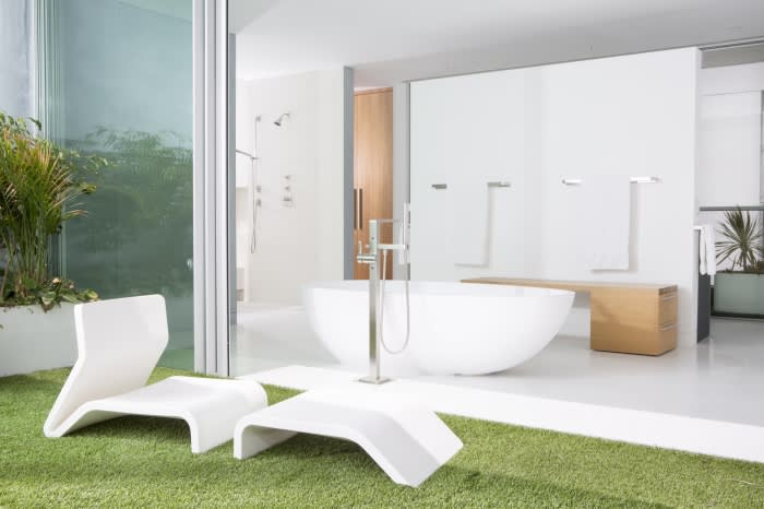 Modern bathroom interior featuring a white bathtub, lounge chairs on artificial grass, and sliding glass doors to an outdoor space.