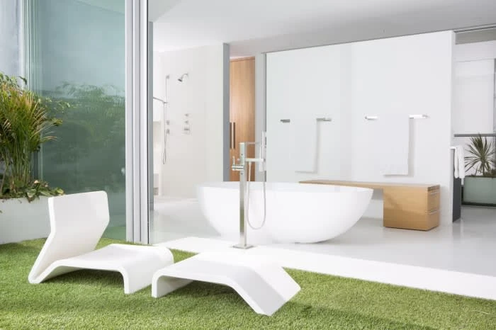 Modern bathroom interior featuring a white bathtub, lounge chairs on artificial grass, and sliding glass doors to an outdoor space.