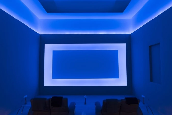 Modern blue-lit home theater featuring comfortable recliner chairs, large screen, and ambient lighting for an immersive viewing experience.