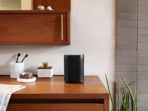 Black speaker sits on a wooden surface in a bathroom setting, complemented by toiletries and decor against a tiled wall.