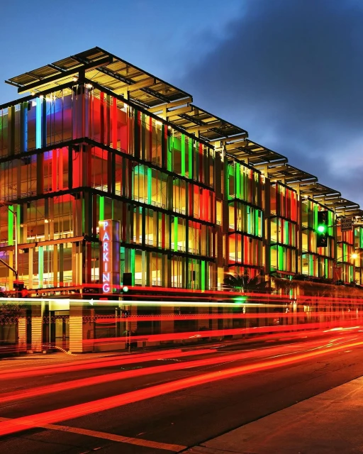Modern parking garage with colorful facade at night, illuminated by internal lights and light trails from passing traffic.