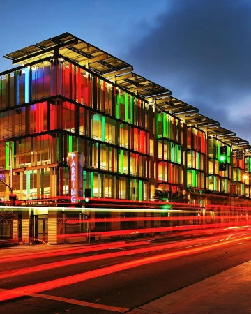 Modern parking garage with colorful facade at night, illuminated by internal lights and light trails from passing traffic.