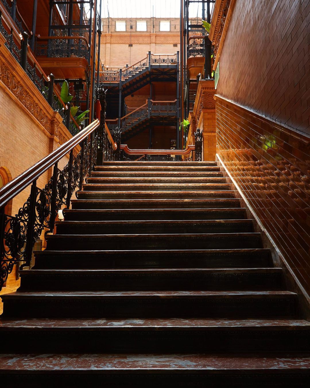 Intricate architecture featuring a central staircase, black ironwork railings, and brick walls in a brightly lit atrium.
