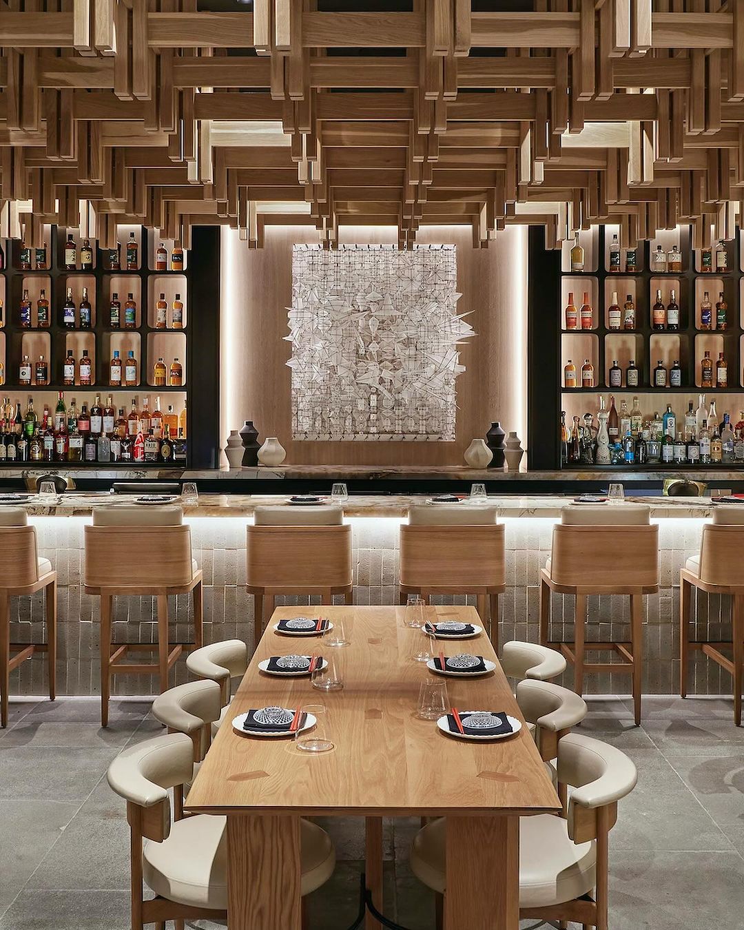 Stylish interior of a restaurant featuring a bar area with stools, a set dining table, wood accents, and displayed liquor bottles.