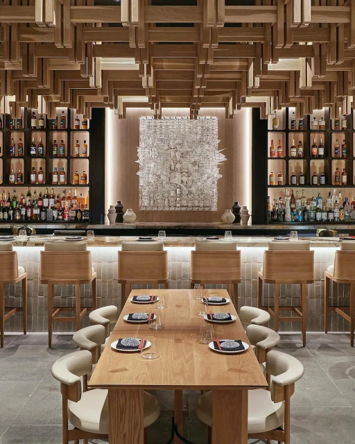 Stylish interior of a restaurant featuring a bar area with stools, a set dining table, wood accents, and displayed liquor bottles.
