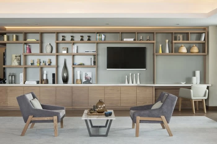 Living room interior with gray armchairs, a marble coffee table, and built-in shelving unit with a television and decorative objects.