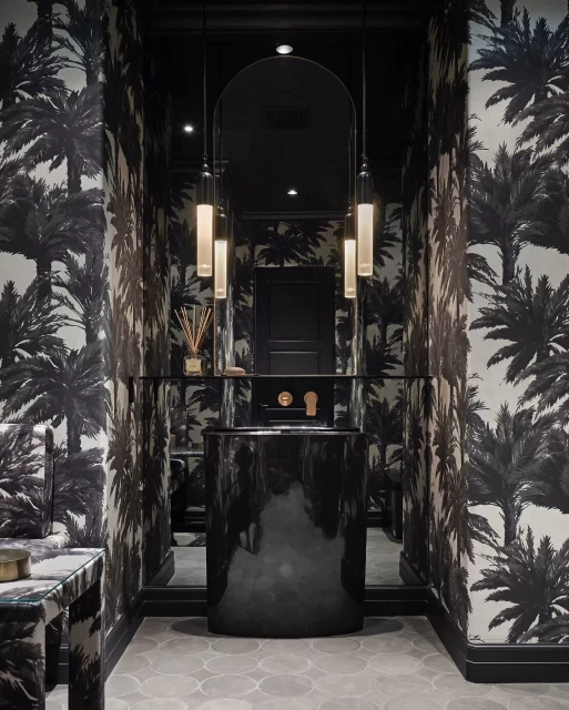 Elegant powder room interior featuring black vanity, cylindrical pendant lights, palm tree wallpaper, creating a stylish and sophisticated space.
