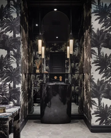 Elegant powder room interior featuring black vanity, cylindrical pendant lights, palm tree wallpaper, creating a stylish and sophisticated space.