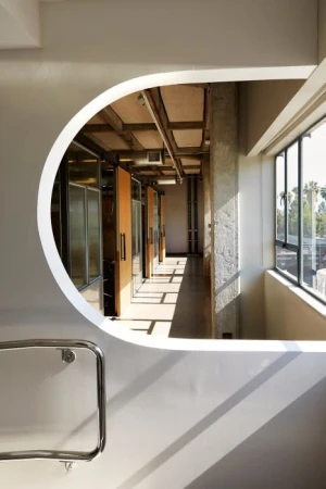 Interior view through an architectural opening reveals a corridor bathed in natural light, with a glimpse of exterior greenery.