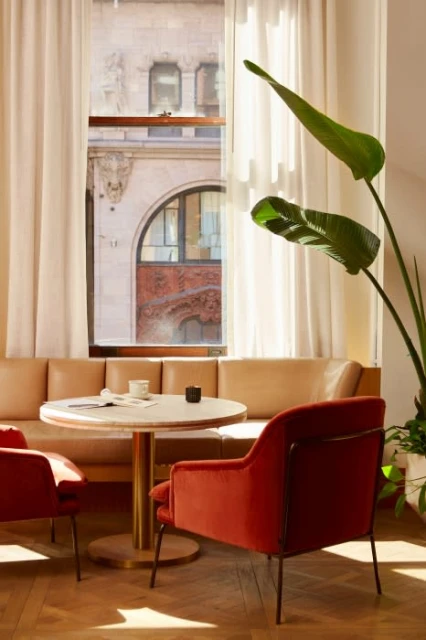 Cozy indoor seating area with modern armchairs, a round table set for two, and a large window with soft, natural light.