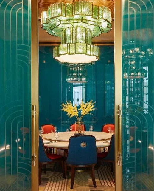 Ornate light fixture illuminates a dining table set with clear glassware and surrounded by colorful chairs in a restaurant setting.
