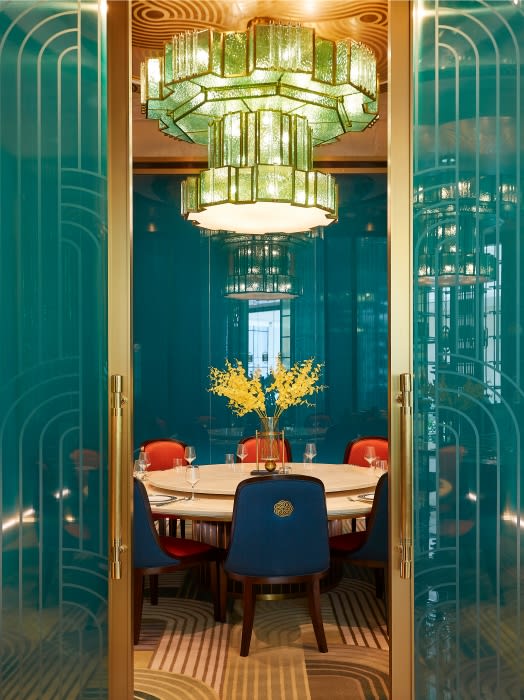 Restaurant dining room with a round table set with dishes and glasses, surrounded by chairs, under a modern chandelier.