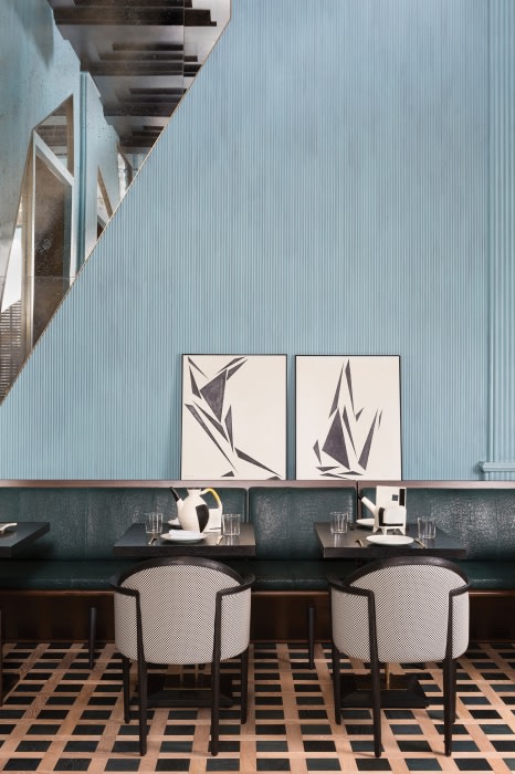 Restaurant interior features seating with chairs and banquette, abstract art, and patterned flooring in a contemporary design setting.