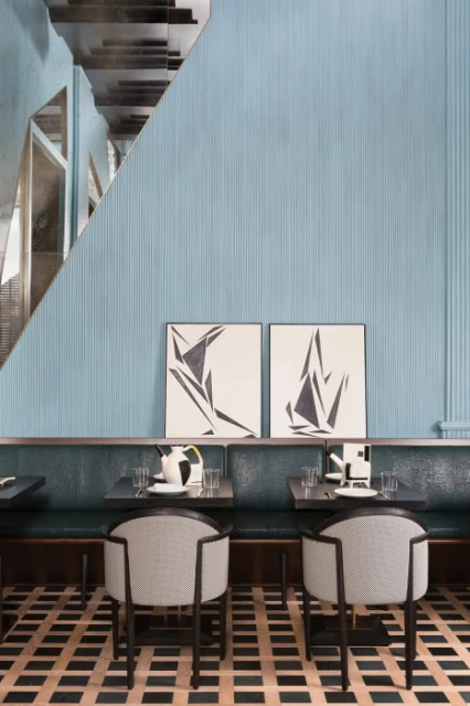 Restaurant interior features seating with chairs and banquette, abstract art, and patterned flooring in a contemporary design setting.