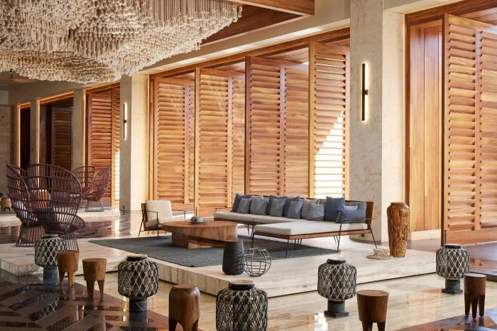 Interior design of a hotel lobby featuring wooden shutters, modern furniture, decorative lamps, and a unique ceiling installation.