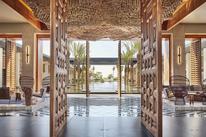 Open wooden doors leading to a luxurious lobby with palm trees visible in the background, showcasing a high-end architectural design.