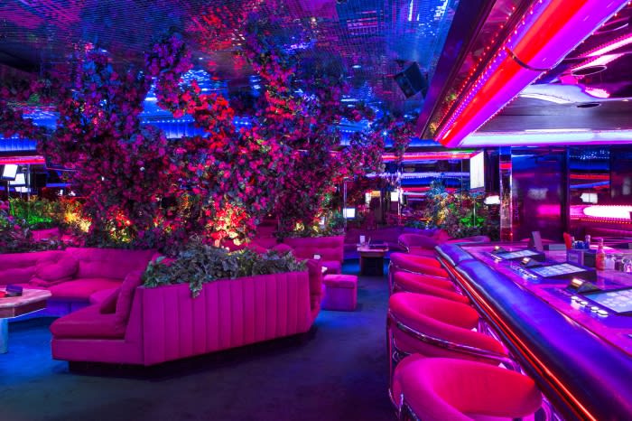 Luxurious nightclub interior with plush pink seating, lush greenery, mirrored ceilings, and vibrant neon lighting creating a unique atmosphere.