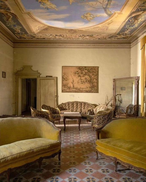 Ornate living room interior featuring vintage furniture, a decorative ceiling fresco, patterned tile flooring, and soft, natural light.