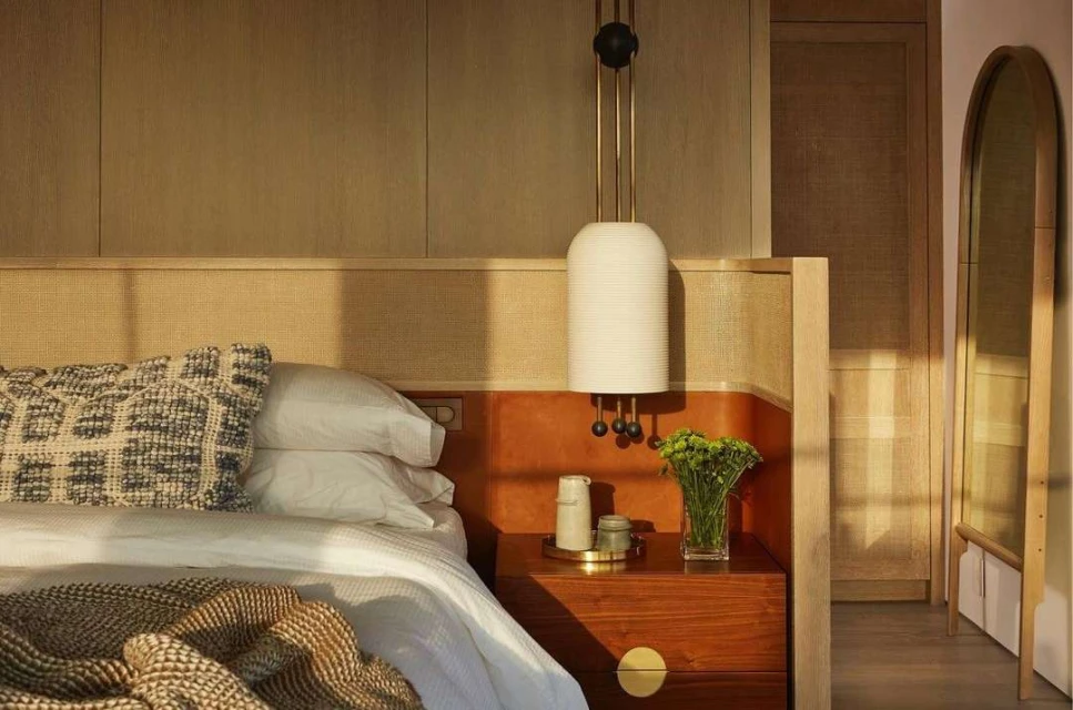 Bedroom interior featuring a bed with patterned pillows and a throw blanket, a wooden nightstand, and a modern hanging lamp.