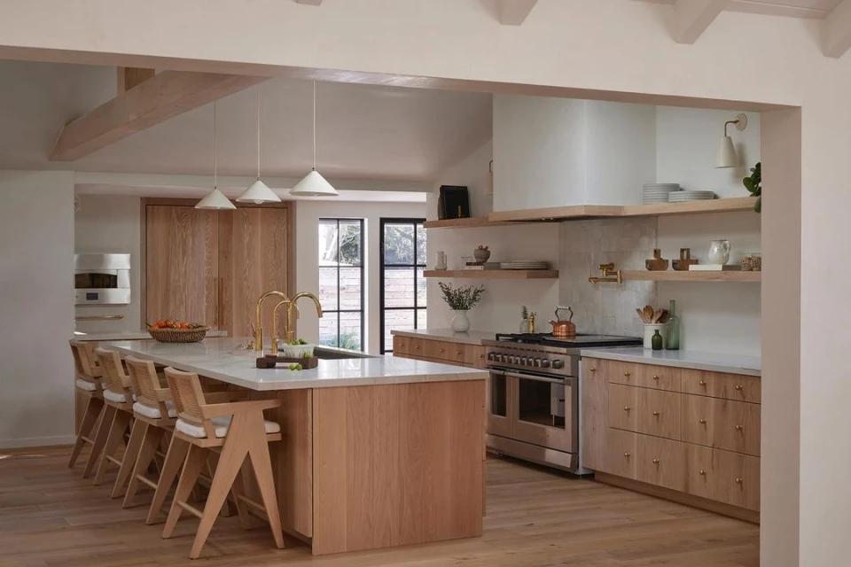 Bright and spacious kitchen interior featuring light wood cabinetry, a marble countertop island with bar stools, and modern pendant lighting.