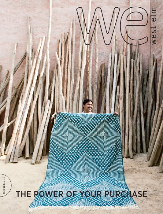 Magazine cover featuring a man holding up a teal and white patterned rug in front of a backdrop of stacked sticks. 'WE' and 'West Elm' logo.