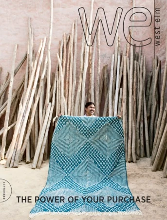 Magazine cover featuring a man holding up a teal and white patterned rug in front of a backdrop of stacked sticks. 'WE' and 'West Elm' logo.