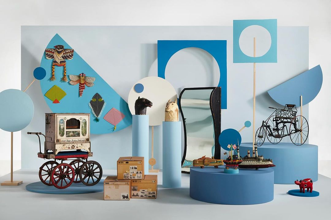 Still life of vintage toys and props in a studio setting. Features a toy organ, model ships, horse busts, and colorful geometric shapes.