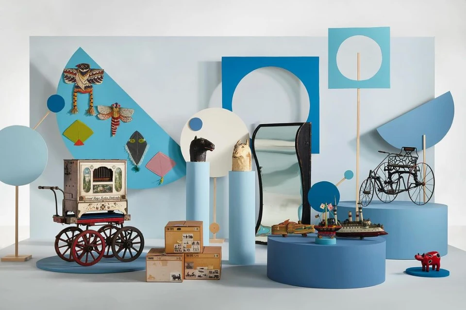 Still life of vintage toys and props in a studio setting. Features a toy organ, model ships, horse busts, and colorful geometric shapes.
