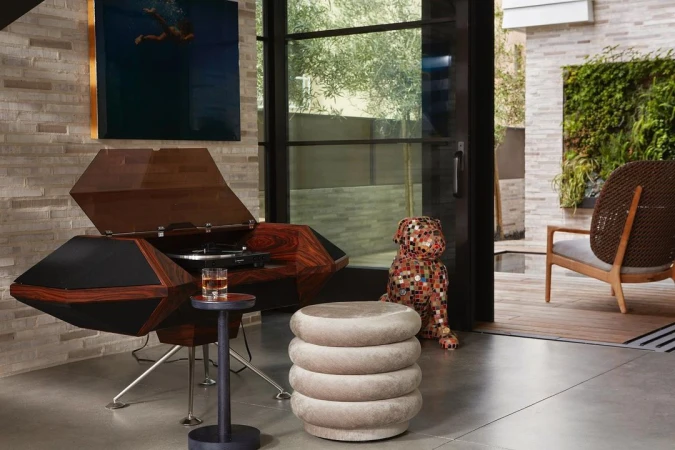 Modern living room interior with sculptural wood audio console, round upholstered stool, and a tiled mosaic dog sculpture.