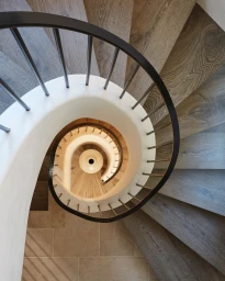 Top-down view of a modern spiral staircase with wooden treads, white curved inner wall, and black metal railings.