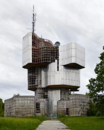 Brutalist architectural structure with metallic panels and exposed grid framing under an overcast sky.