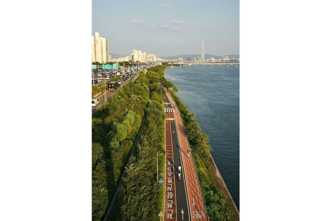 Aerial view of a city park and walkway with distant skyscrapers in Seoul, South Korea, along the Han River during daylight.