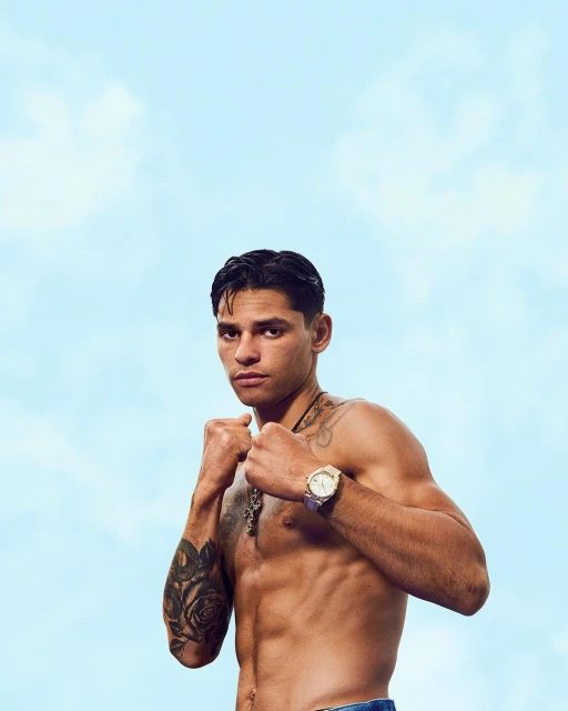 Portrait of a shirtless man with a muscular build posing with his fists up against a light blue sky with faint clouds.