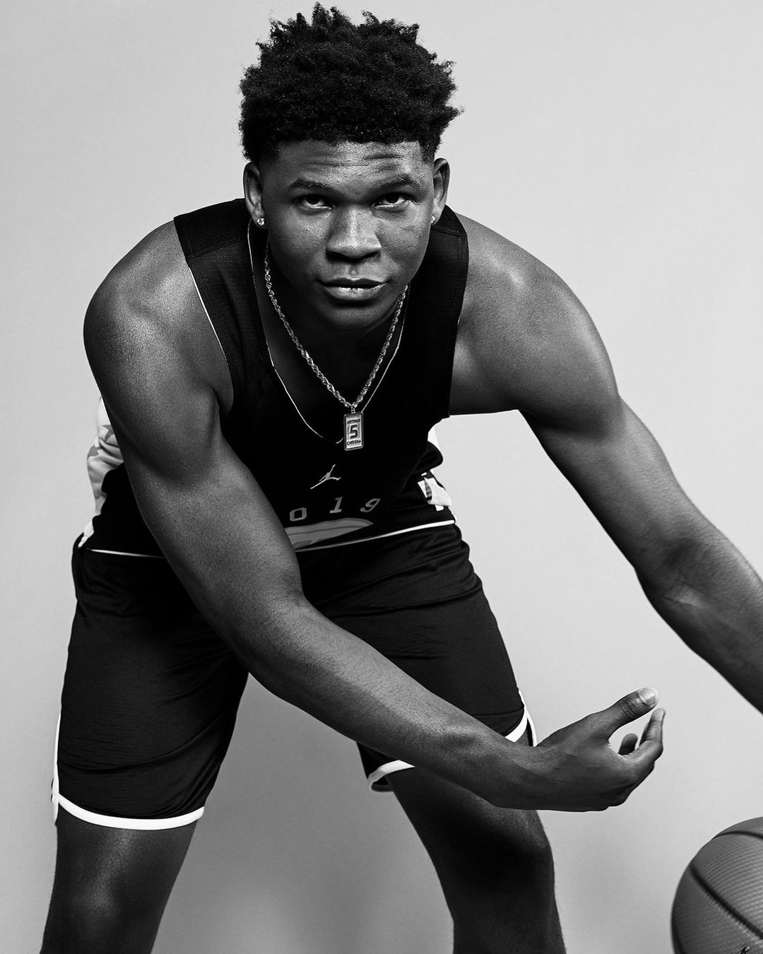 Monochrome portrait of a muscular African-American athlete in sports attire with a basketball, standing in a light grey studio.