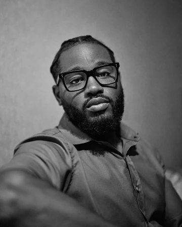 Monochrome portrait of a black man wearing thick-rimmed glasses and a collared shirt, captured by photographer Ryan Young.