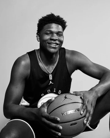 Portrait of Anthony Edwards smiling while holding a basketball, wearing a tank top against a plain studio background.