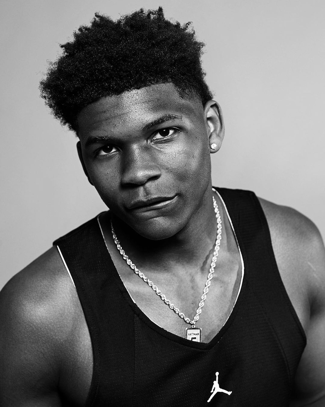 Portrait of a young Black man wearing a black tank top and a silver chain necklace against a light background